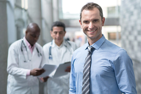 healthcare administrator smiling at camera in front of two doctors looking at charts
