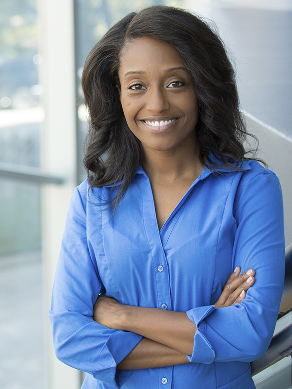 Behavior analysis professional smiling at camera while standing indoors in front of a large window wall.