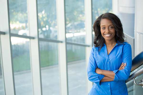 Behavior analysis professional smiling at camera while standing indoors in front of a large window wall.