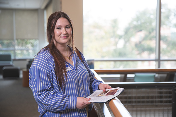 Student looking at camera while holding a small stack of papers.