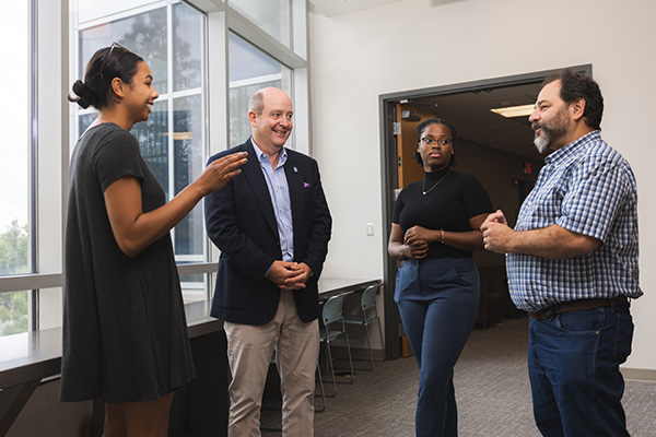 UWF business professor conversing with three UWF MBA students.