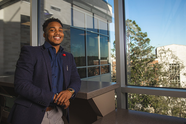 Student in professional attire smiling at camera in front of a window in Building 76A on the UWF Pensacoal campus.