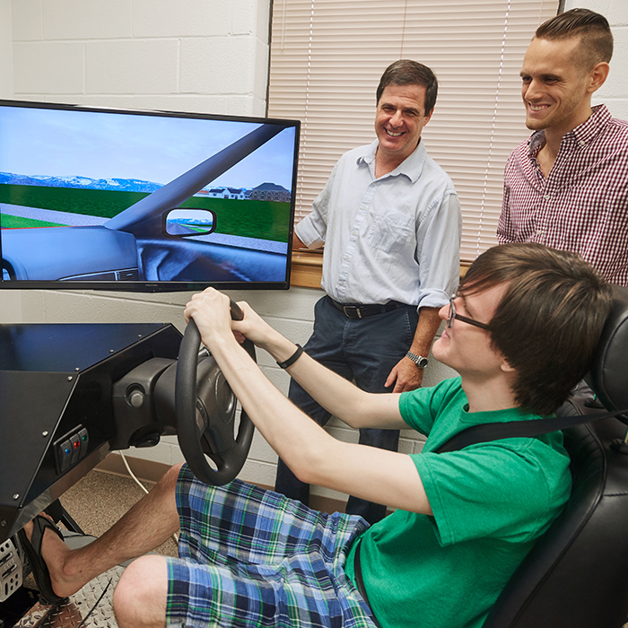 Psychology student takes a spin in the Driving Simulator as a graduate student and Professor record the results.
