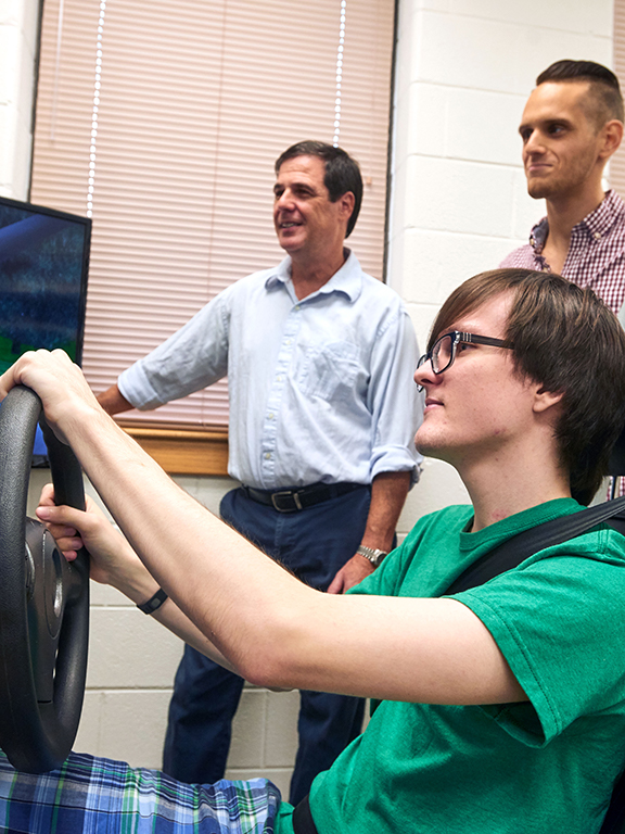 Psychology student takes a spin in the Driving Simulator as a graduate student and Professor record the results.	